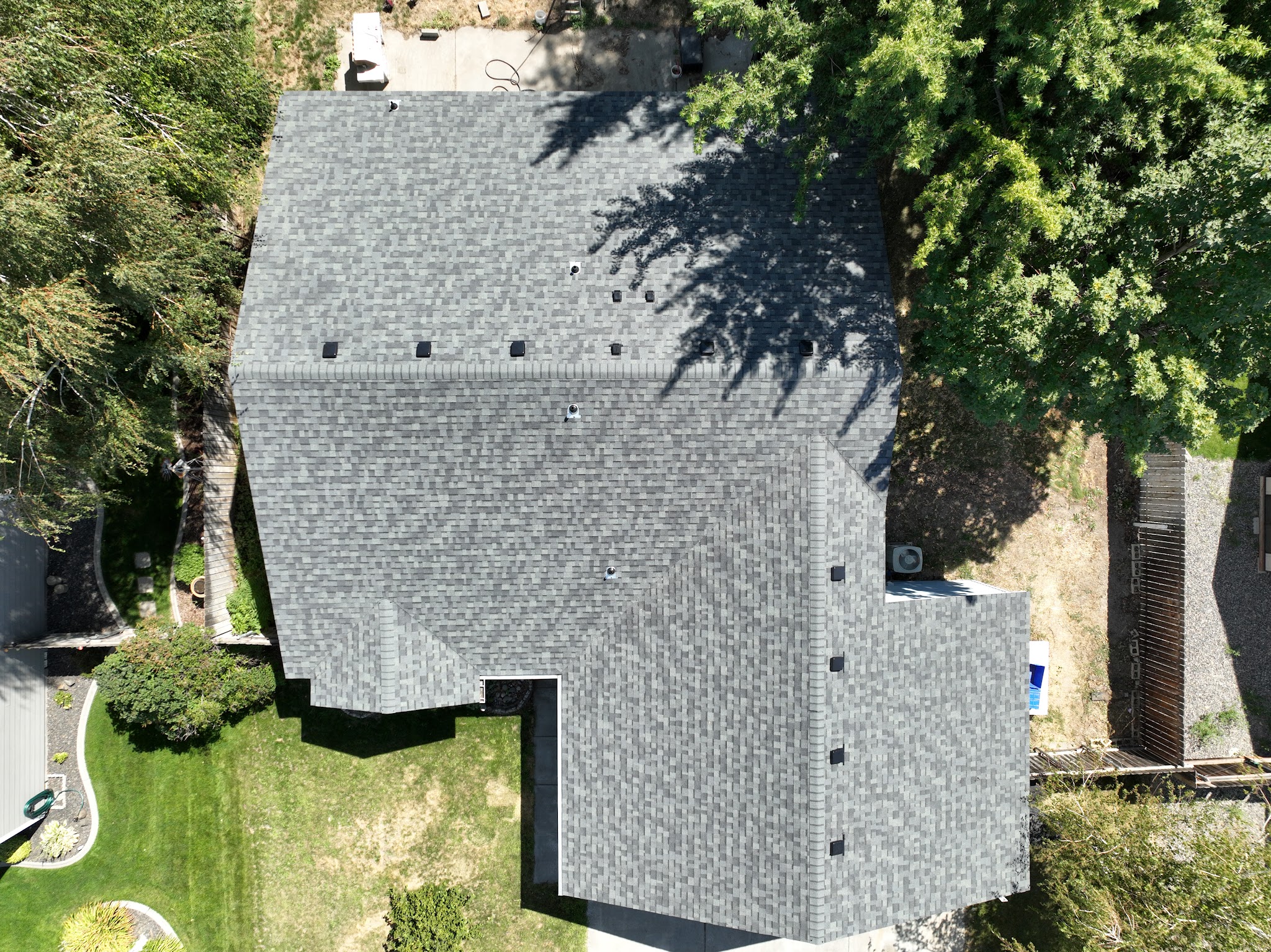 Aerial view of a finished shingle roof near a residential street with an American flag visible
