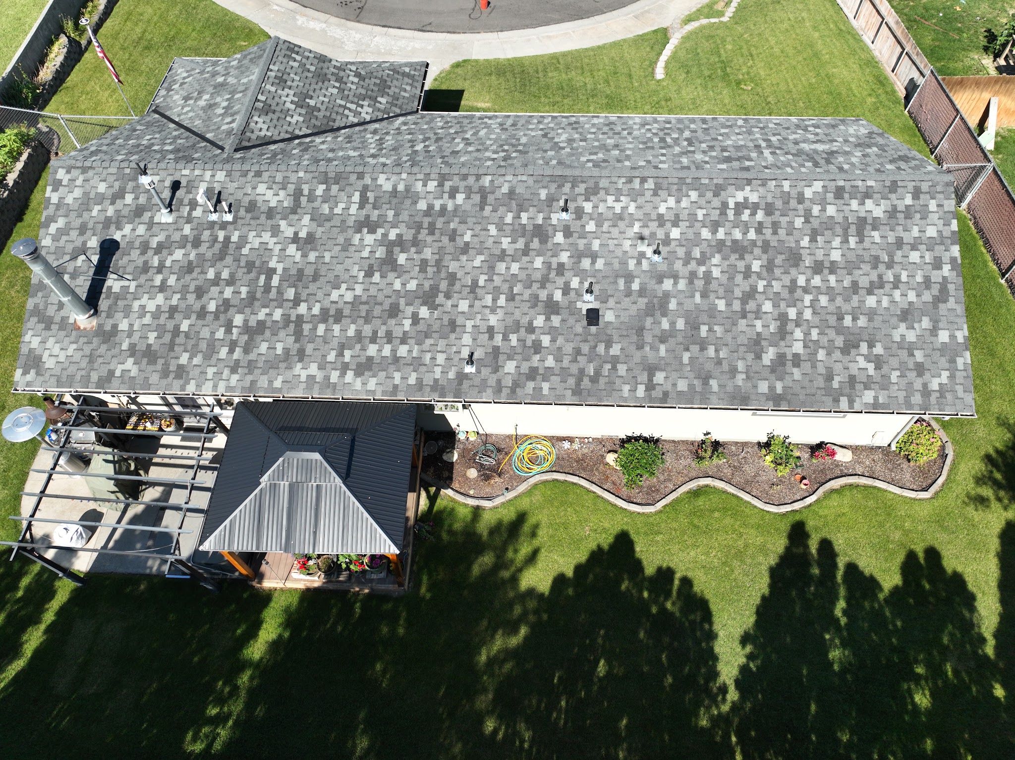 Aerial view of a gray shingle roof with vent boots and a landscaped backyard below